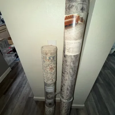 Two rolled modern area rugs, including a Hathaway area rug and an Everwash washable area rug, leaning against a wall.