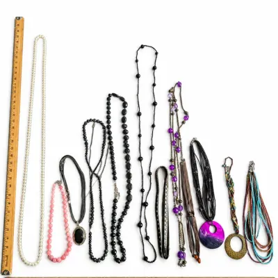 Collection of assorted fashion necklaces and chokers in various materials, colors, and styles arranged with wooden yardsticks for scale.