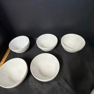 Set of five simple white ceramic cereal or soup bowls shown with a wooden yardstick for size measurement.