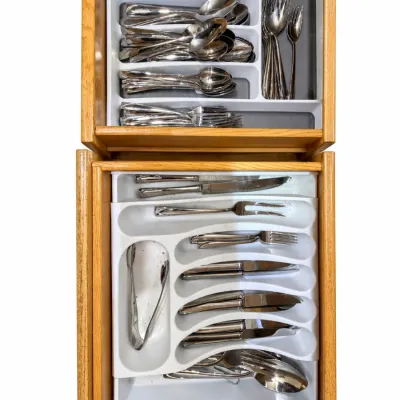 Large collection of stainless steel flatware and serving utensils neatly arranged in white plastic drawer organizers within two oak drawers.