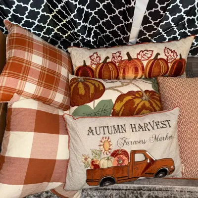 Assortment of autumn-themed decorative throw pillows, featuring pumpkin motifs, plaid patterns, and a harvest truck design.