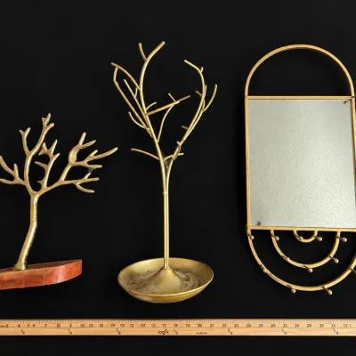 Collection of modern brass-tone metal jewelry displays, including two tree-shaped organizers and a wall-hanging mirror with hooks.