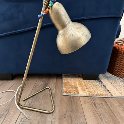 Brushed antique brass desk lamp featuring a triangular base and an adjustable bell-shaped shade, adorned with a colorful beaded strand.