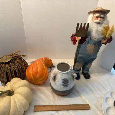 Autumn table decor assortment including faux pumpkins, a decorative gourd, a rustic ceramic vessel, and a standing farmer Santa figure.