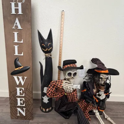Collection of Halloween decor including a wooden 'Happy Halloween' porch sign, a tall carved black cat figure, and two dressed...