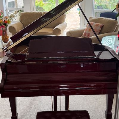 Polished mahogany baby grand piano with matching tufted leather bench, set in a bright living room.