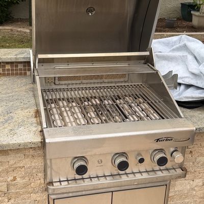 Built-in Turbo Elite stainless steel outdoor BBQ grill with an open hood, warming rack, and ceramic briquettes.