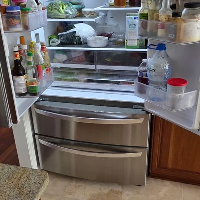 Modern stainless steel french door refrigerator with bottom freezer drawers, fully stocked and illuminated.