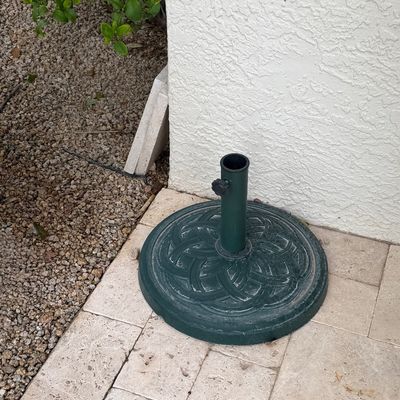 Dark green cast metal patio umbrella base featuring a round form with a textured basketweave pattern and tightening knob.