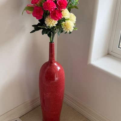 Tall, red speckled ceramic bottle-style floor vase filled with colorful artificial flowers including pink carnations and cream...