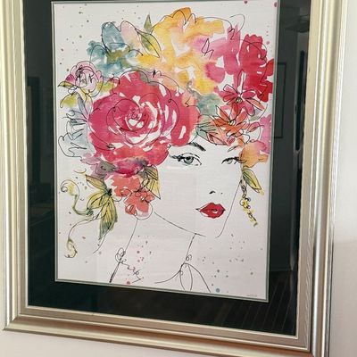 Framed fashion illustration print featuring a woman with a vibrant floral headpiece, mounted with a black mat and silver-tone frame.