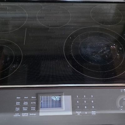 Modern black glass smooth-top electric cooktop featuring a digital touch-control front panel and multiple burner zones.