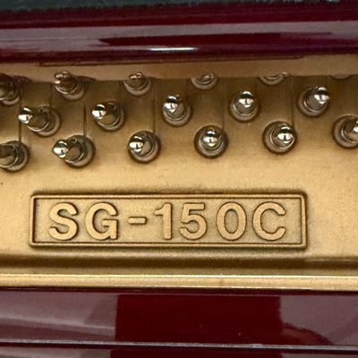 Detail view of a grand piano interior showing tuning pins and model number SG-150C stamped on the harp frame.
