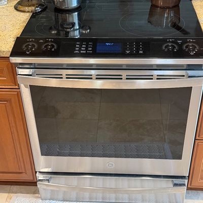 GE stainless steel slide-in electric range featuring a glass cooktop, front control panel, and storage drawer below.