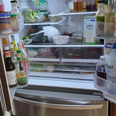 Modern stainless steel French door refrigerator with bottom freezer drawers, fully stocked and illuminated.