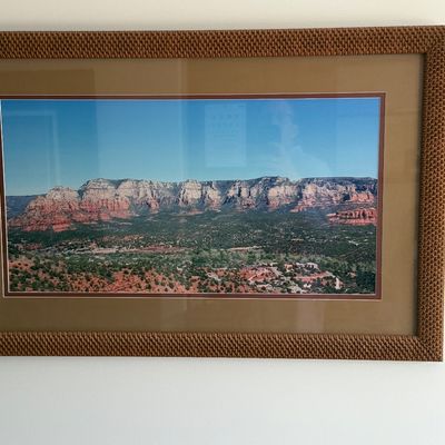 Framed panoramic landscape print depicting red rock formations, presented under glass with a double mat and a textured woven-style frame.