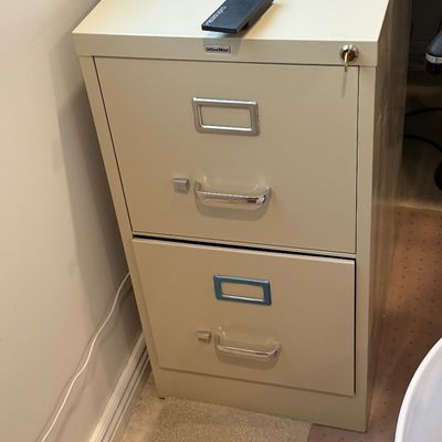 OfficeMax two-drawer metal filing cabinet in beige, featuring silver-tone handles, label holders, and a key inserted in the top lock.