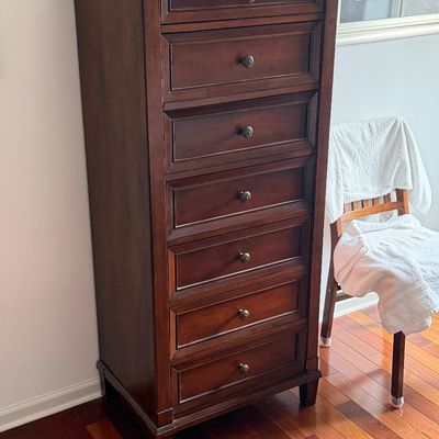 Tall dark wood lingerie chest featuring seven drawers with molded panel fronts and brass knobs.