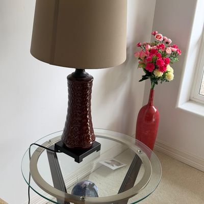Contemporary table lamp with a textured reddish-brown ceramic base and neutral fabric drum shade, sitting on a round glass-top accent table.