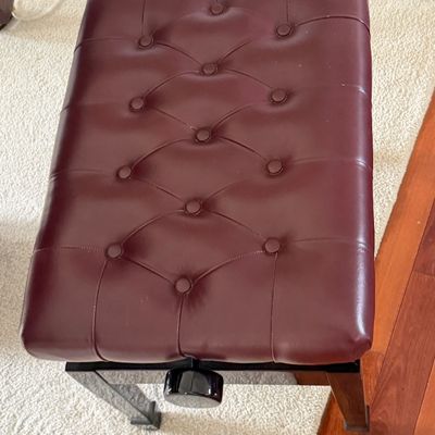 Adjustable piano bench featuring button-tufted burgundy vinyl upholstery and a black lacquered base.