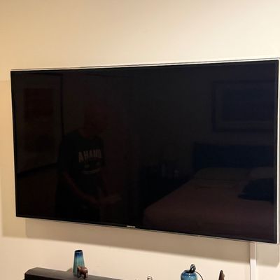 Large wall-mounted Samsung flat screen television with slim silver bezel, shown above a soundbar and media console with decor.