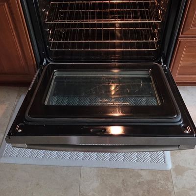 Modern black and stainless steel slide-in electric range with the oven door pulled open, revealing multiple wire racks and an interior...