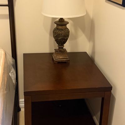 Dark wood square nightstand paired with a ornate classical-style urn table lamp topped with a off-white shade.
