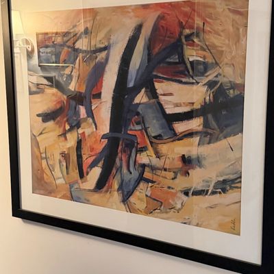 Large framed abstract expressionist print featuring dynamic brushstrokes in warm earth tones, blue, and black, matted in a black frame.