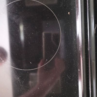Black glass cooktop surface with visible heating zone rings, showing light dust and smudges.