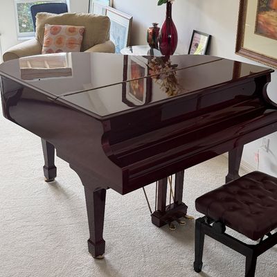 Polished mahogany baby grand piano accompanied by a matching tufted leather bench, featuring a high-gloss finish and three brass pedals.