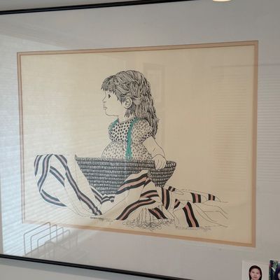 Framed ink drawing print of a young girl in a woven basket, signed and dated 1987 in the lower right corner.