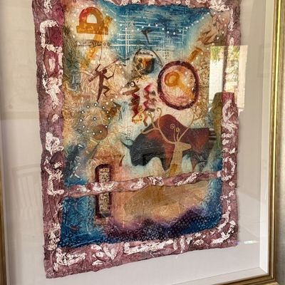 Framed mixed-media artwork featuring abstract, cave-art-inspired motifs on textured paper, housed in a thin metallic gold-tone frame.