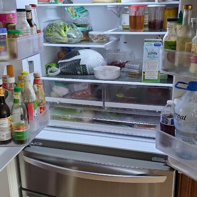 Modern stainless steel French door refrigerator with two freezer drawers, shown open and fully stocked.