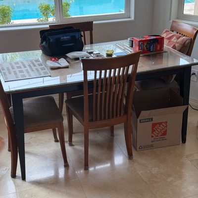 Modern dining set with a glass-top table, dark painted frame, and matching wooden slat-back chairs with cushioned seats.