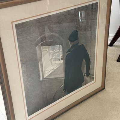 Large framed wall art print featuring a figure in a dark jacket looking toward a window, presented in a wooden frame with a double mat.