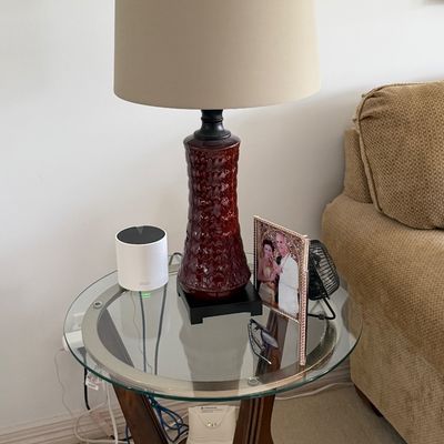 Round glass-top side table with wooden legs, topped with a burgundy textured ceramic table lamp and a beige fabric shade.