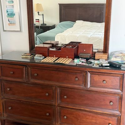 Traditional wooden bedroom dresser with large attached mirror and multiple storage drawers, displayed with small collectibles on top.