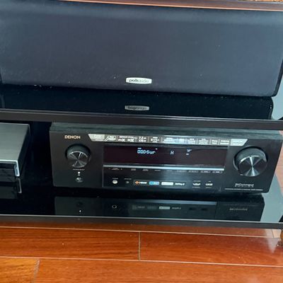 Denon IN-Command series audio receiver set on a glass entertainment shelf below a Polk Audio center channel speaker.