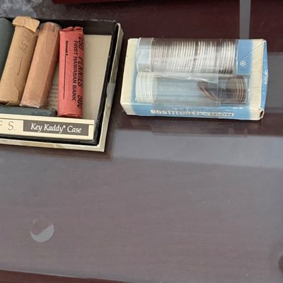 Collection of rolled and plastic-tubed coins, including paper-wrapped pennies from First Hawaiian Bank, housed in small display boxes.