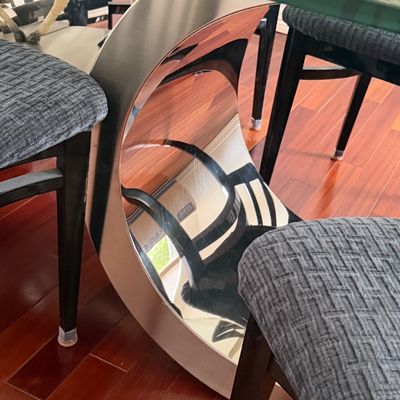 Contemporary dining set featuring a thick glass-top table with a polished chrome curved base, surrounded by black dining chairs with...