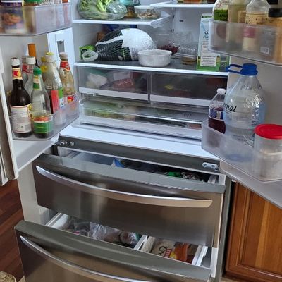 Modern stainless steel French door refrigerator with two bottom freezer drawers, shown fully stocked and open.