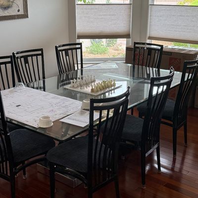Modern glass-top dining table with a dark frame and eight matching high-back chairs with cushioned seats.