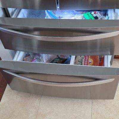 Modern stainless steel french-door refrigerator featuring two pull-out freezer drawers filled with stored goods.