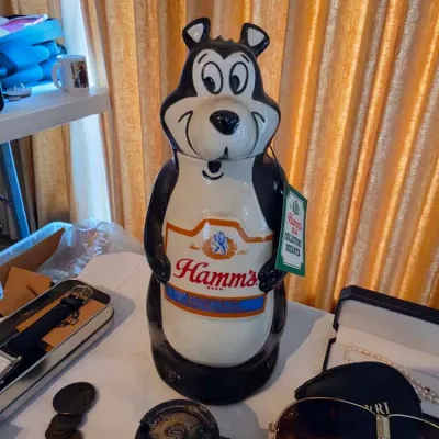Vintage ceramic Hamm's Beer Bear collector's decanter with original hanging tag, set alongside coins and sunglasses.