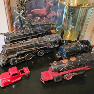 Sale Photo Thumbnail #114: Collection of vintage metal toy train locomotives and a red toy truck cab, displayed alongside a Canadian Mist mirror and a brass lantern.