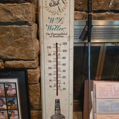 Vintage W.L. Weller advertising metal thermometer featuring a horse head illustration, displayed alongside a golf putter and framed...