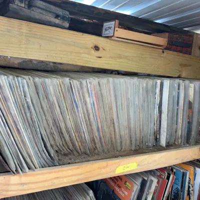 Sale Photo Thumbnail #79: Large collection of vintage vinyl LP records in protective sleeves, stored tightly on wooden shelves.