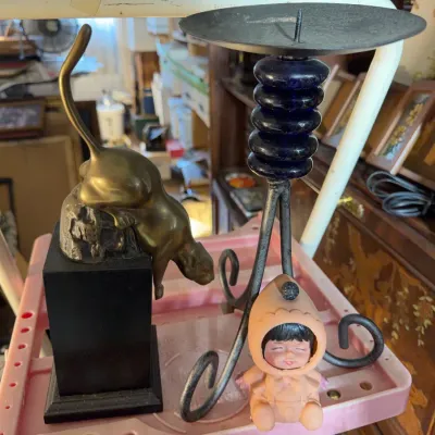 Sale Photo Thumbnail #165: Collection of decorative items including a brass cat statue on a pedestal base, a wrought iron and cobalt blue glass candle holder, and a small vintage rubber baby figure.