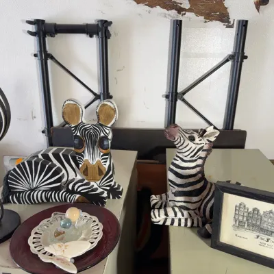 Sale Photo Thumbnail #133: Collection of decorative items featuring two hand-painted zebra figurines, a spiral metal sculpture, a small framed illustration of Five Flies in Amsterdam, and decorative plates with marbles.