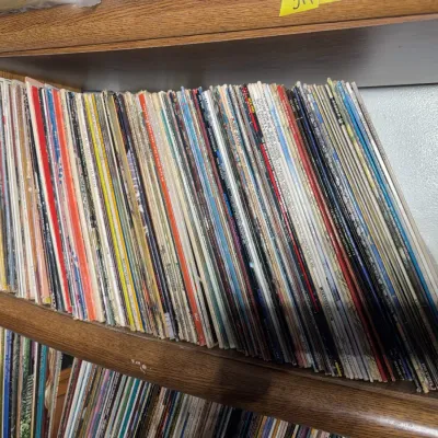 Sale Photo Thumbnail #105: Large collection of vintage 33 RPM vinyl record albums, stored vertically on a wooden bookcase shelf.